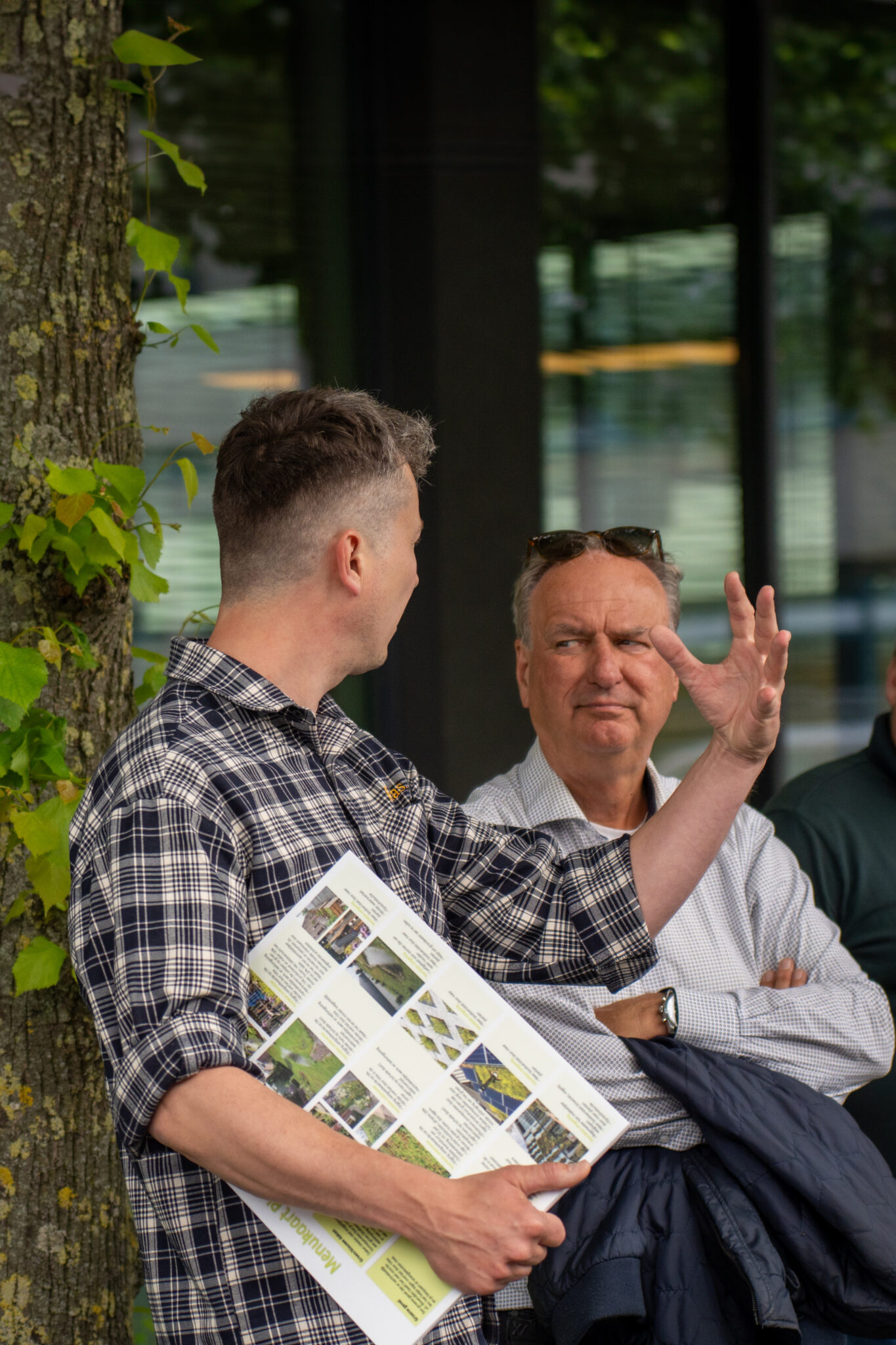 Twee mensen in een groene omgeving praten met elkaar en één man beweegt hierbij zijn hand om iets kracht bij te zetten