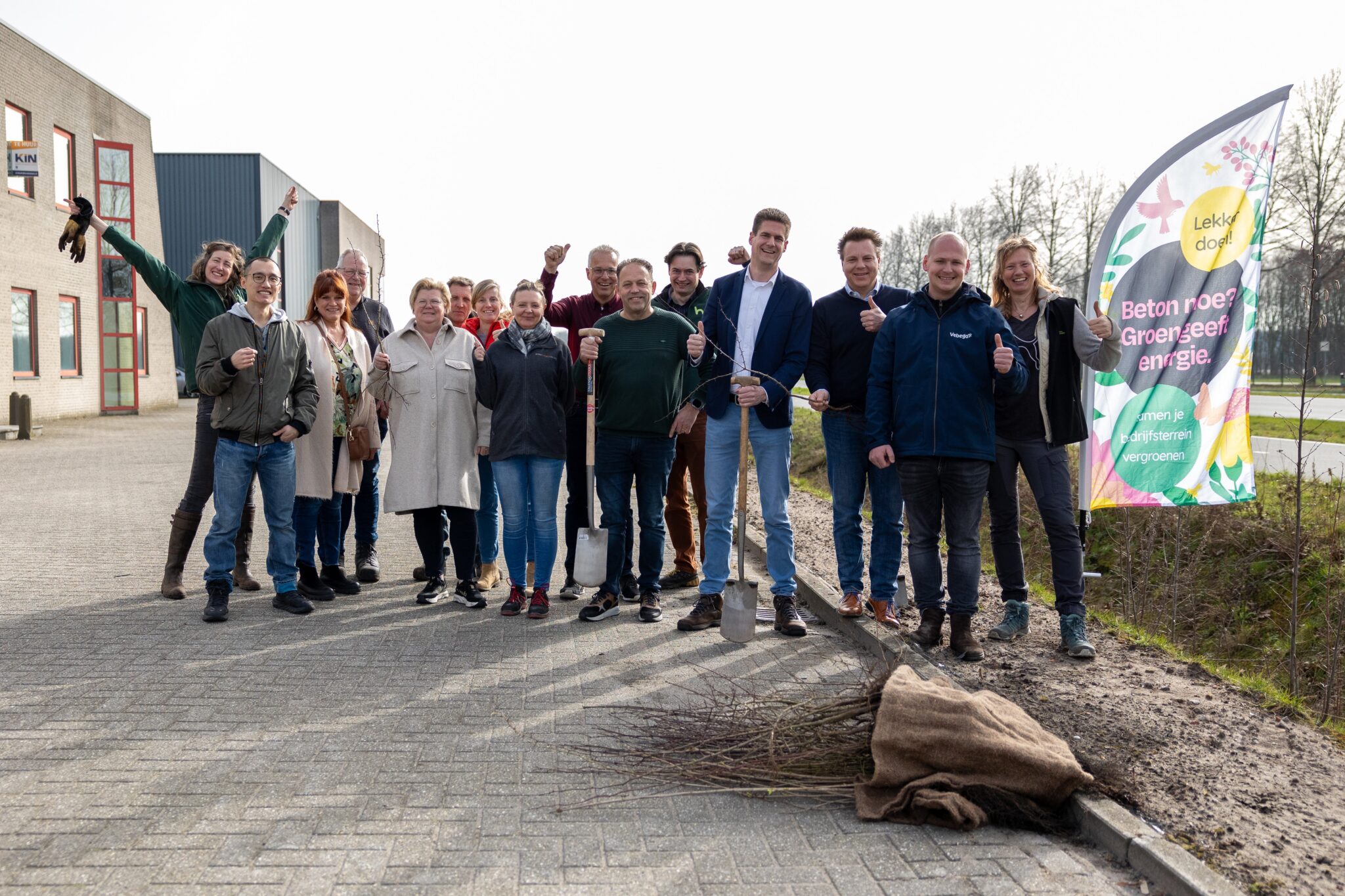 Mensen die een heg hebben geplant poseren blij voor de foto met een vlag van Groen Geeft Energie