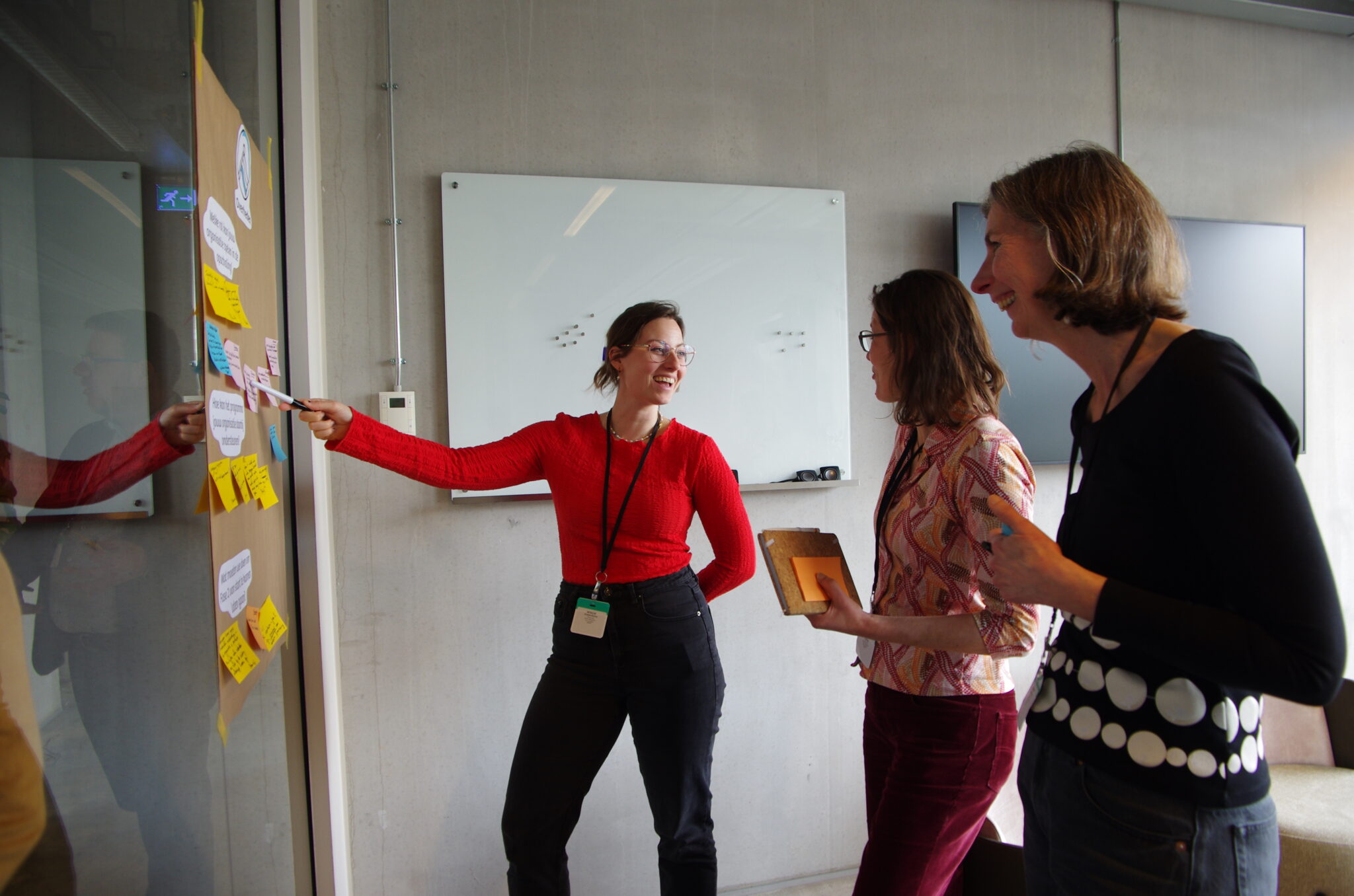 Drie mensen staan bij een poster en plakken post-its tijdens een vergadering